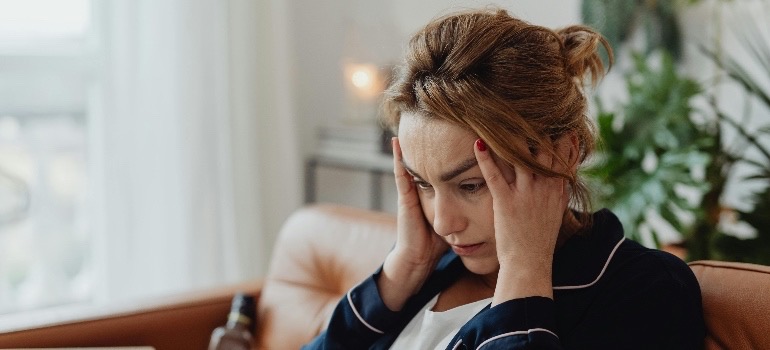 A worried female person holding their head in a bright room, realizing that meth use can cause mental illness