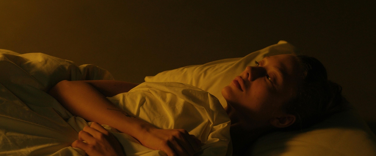A person lies peacefully in bed, their arm draped over soft white sheets, illuminated by warm, soft lighting.
