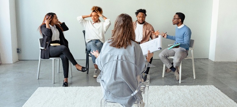 Four people in a group therapy session and a therapist.