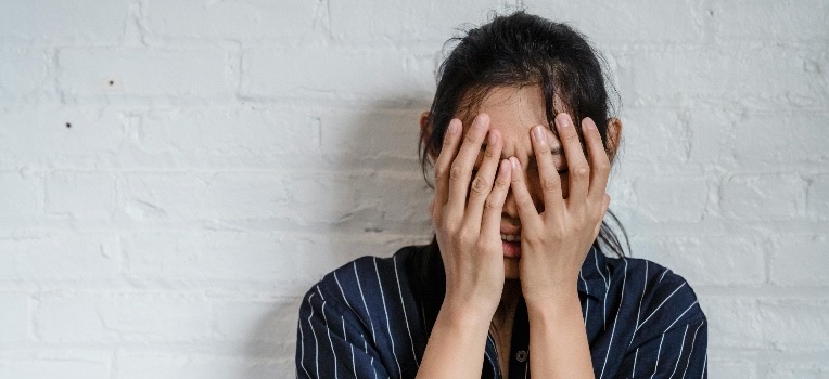 A woman in a blue shirt, hiding her face with her hands